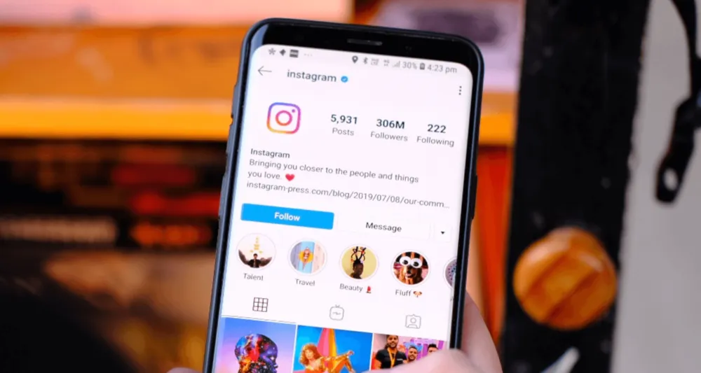 Mão segurando um celular exibindo o perfil do Instagram no aplicativo