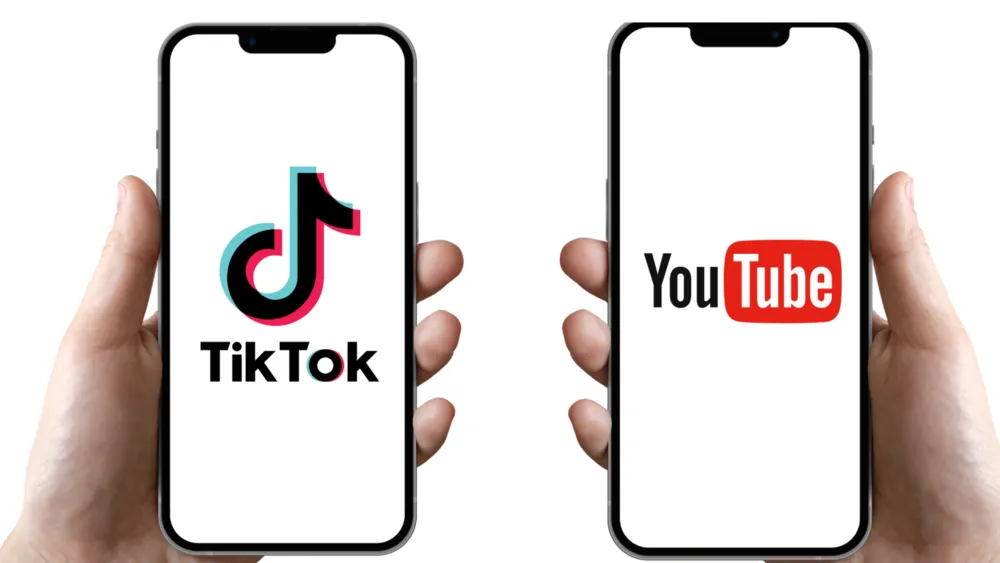 Duas mãos seguram celulares lado a lado, exibindo os logos do TikTok e do YouTube